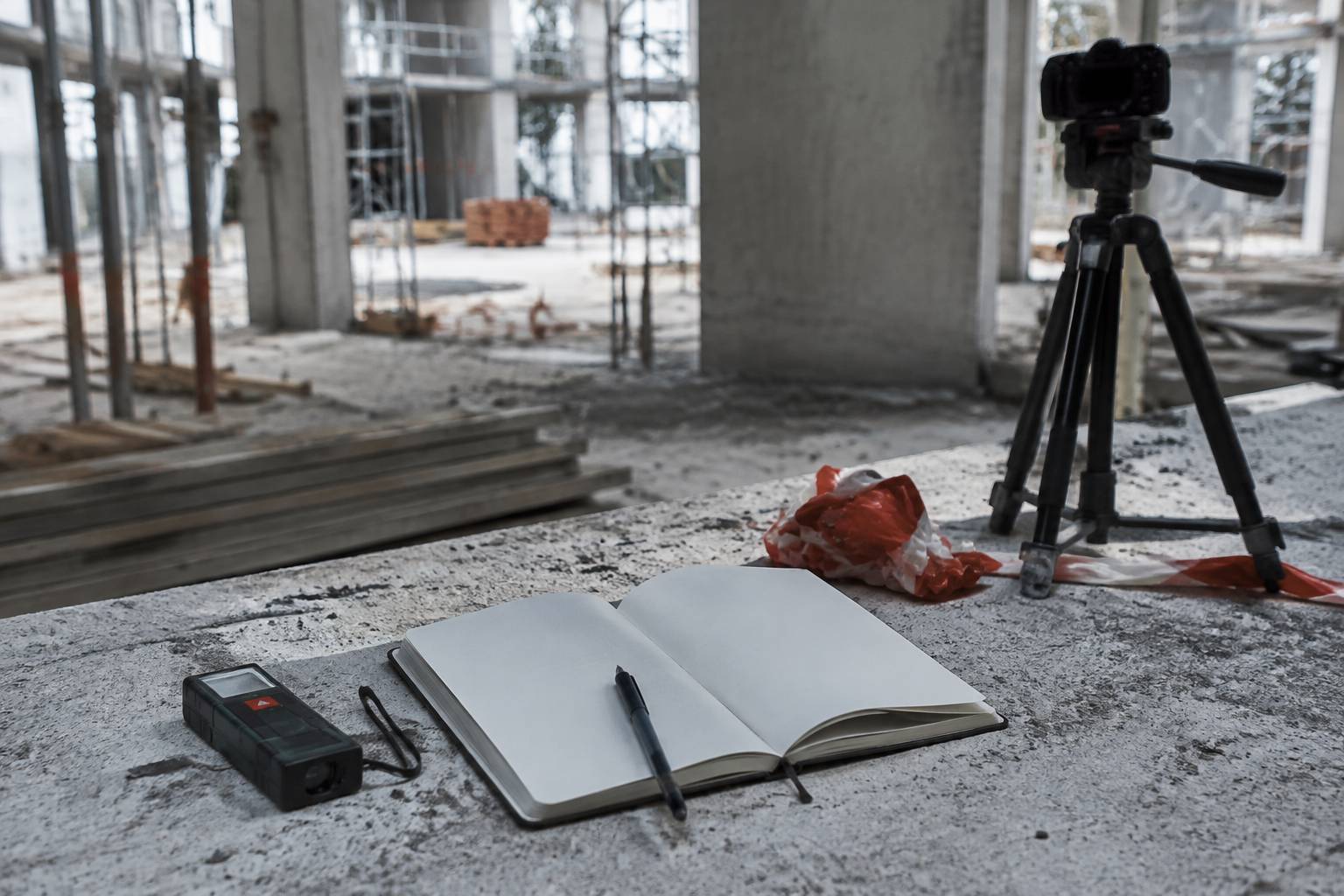 Mètre laser, carnet et appareil photo sur trépied posés sur une dalle de chantier